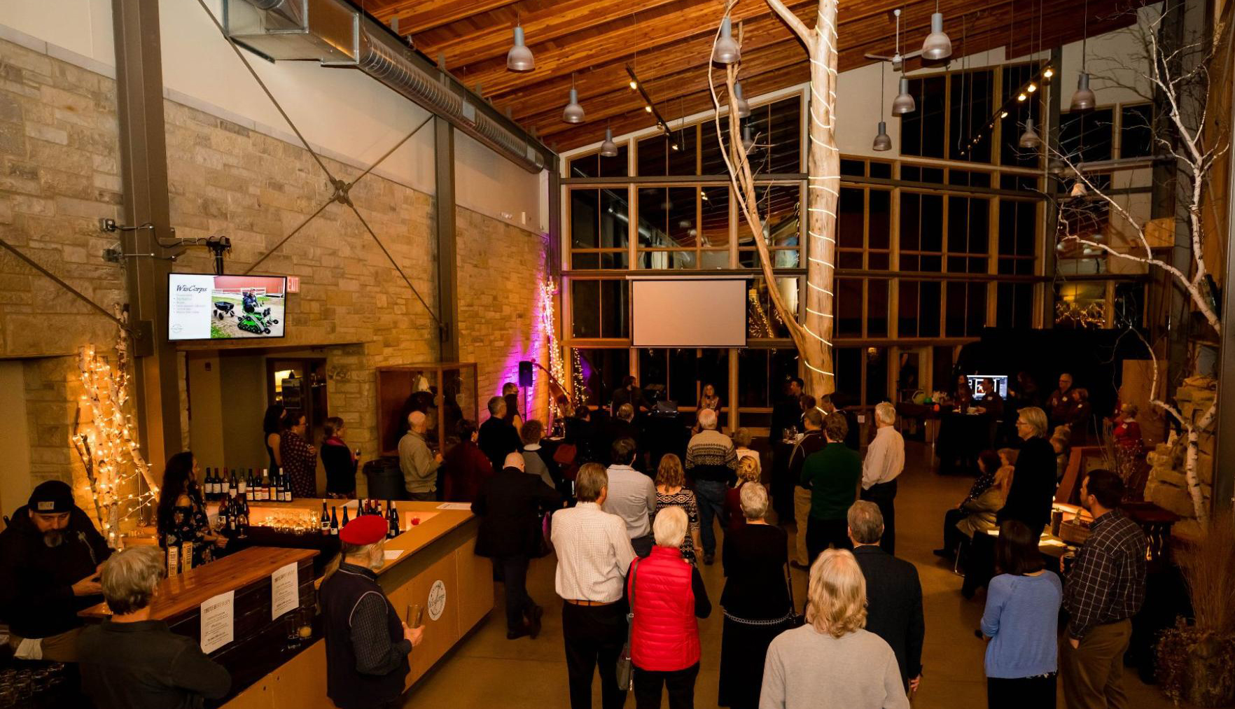 Photo Credit: Ladybug Photography Photo Description: The Atrium is filled with people for a late-night event. Lights are strung zig-zagged across the whole room, and the front desk has been turned into a bar area.