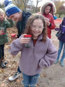 Young girl outdoors showing off bug jar with captured critters