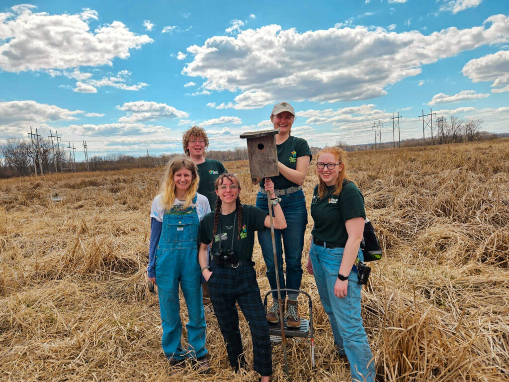 5 americorps members posing around a birdhouse in the prairie