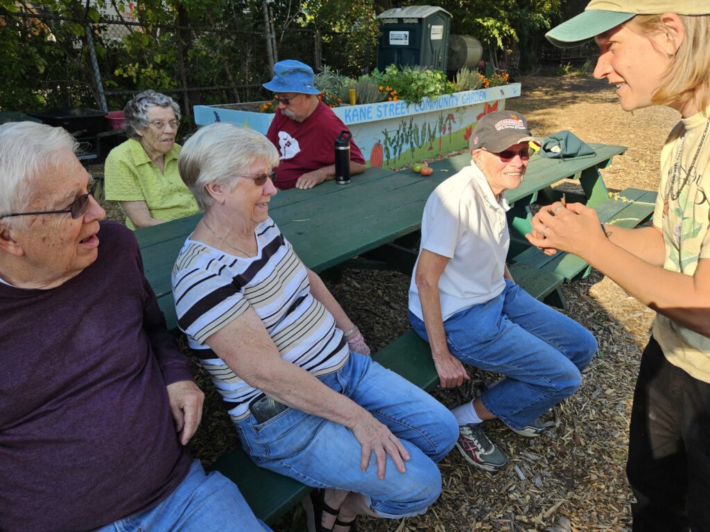 An AmeriCorps Member at The Nature Place shows a group of 4 elderly community memebers the Monarch butterfly's wing with the tag on it. 