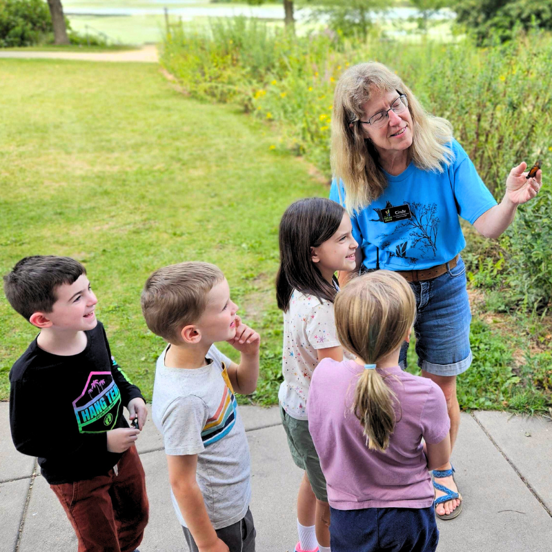 Cindy gently holds a monarch butterfly to tag it's wings in front of a group of elementary students. 