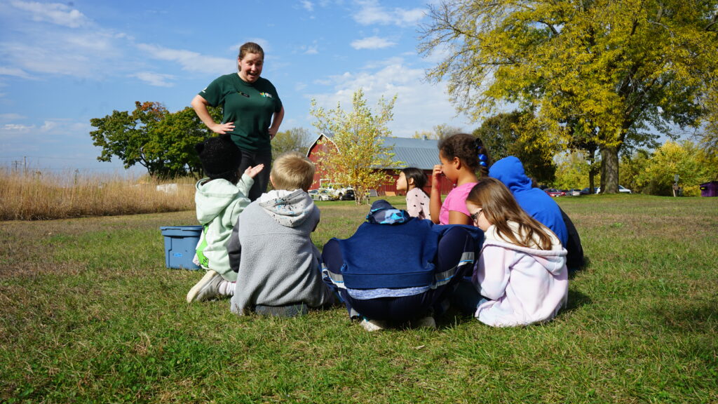 A girl teaching a group of young students outside in the grass.