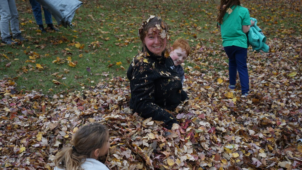 A girl smiling at the camera in a large pile of leaves.