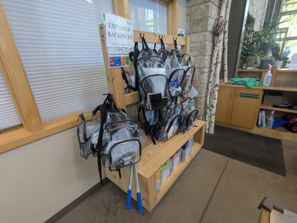 Many clear backpacks hanging on a wooden stand.